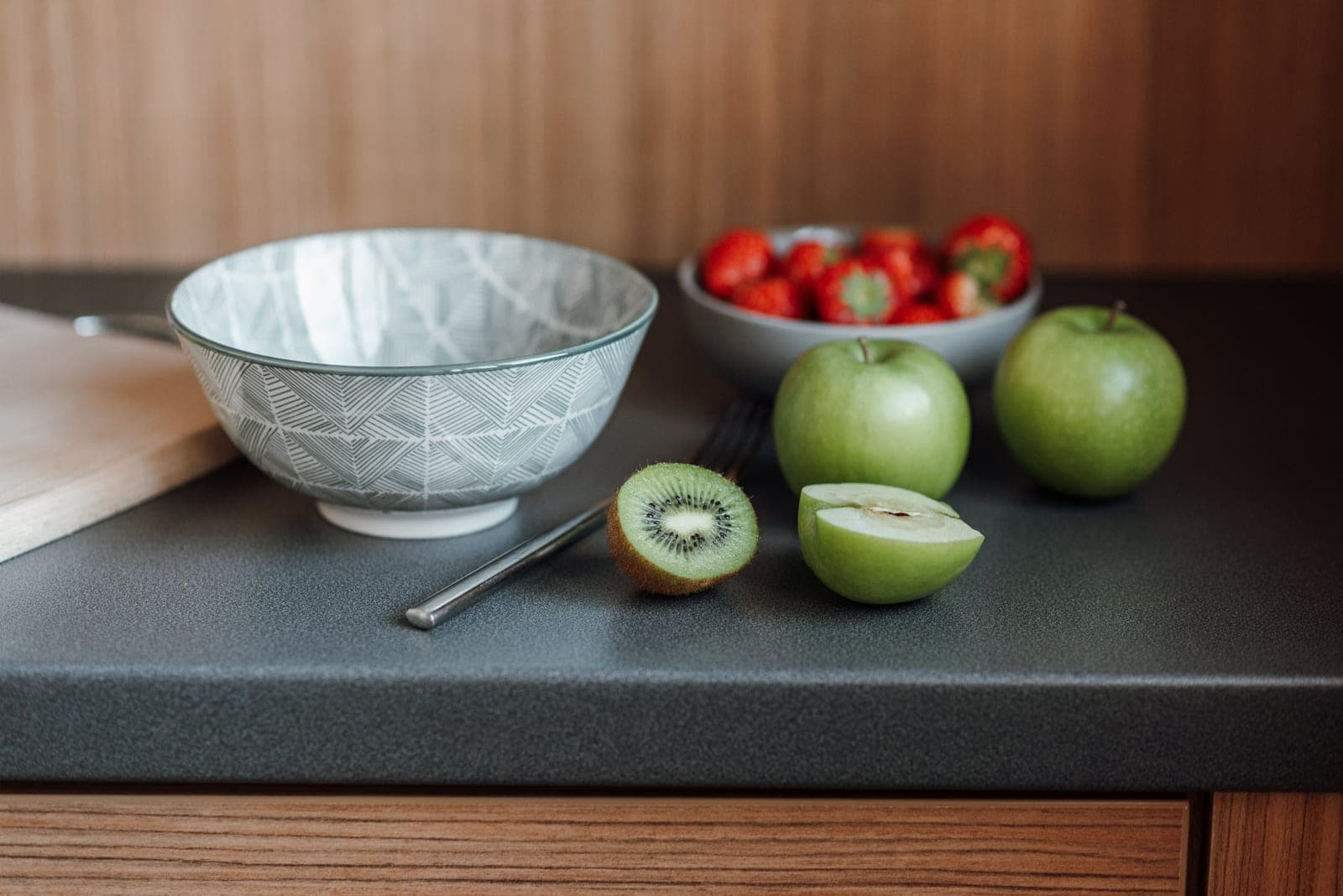 Apples, kiwi and strawberries on a kitchen table beside a cutting board