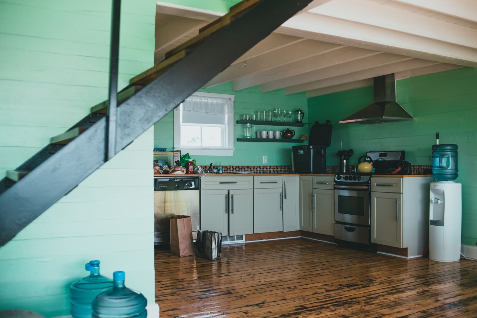 A modern kitchen with green walls, a wooden floor and steel appliances