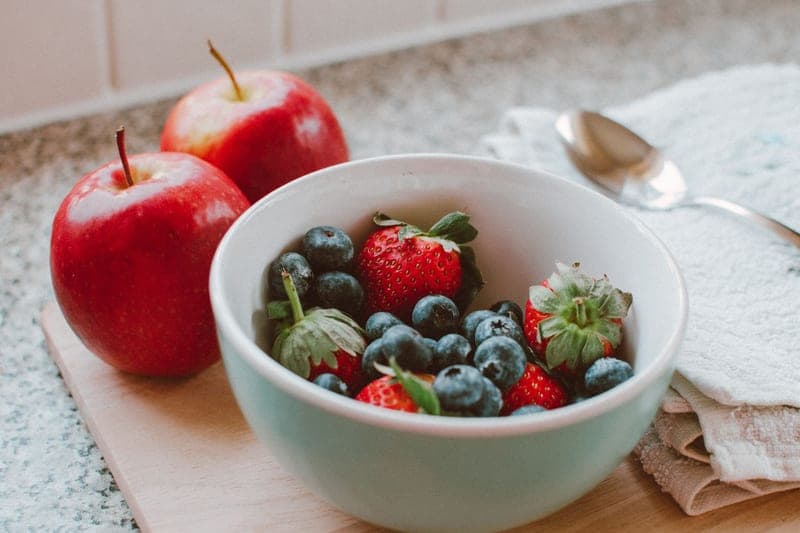 A bowl of fresh berries and apples on a wooden board